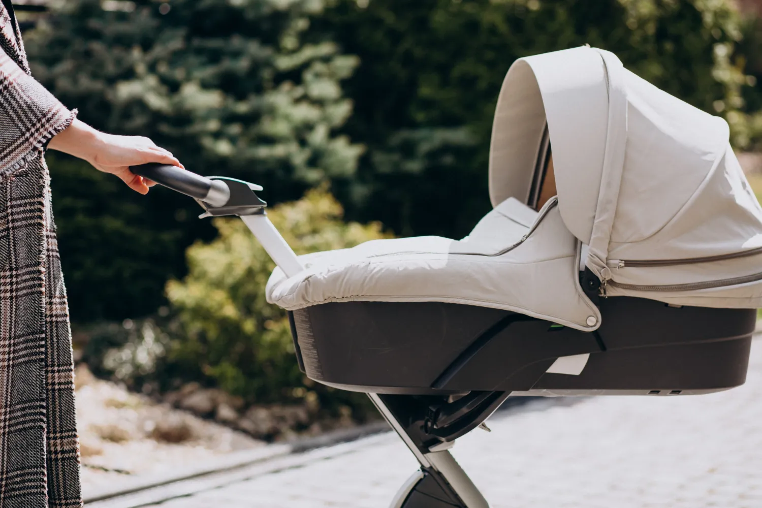 Carrito de bebé moderno en un entorno natural, con una mano agarrando el manillar, ideal para paseos al aire libre.