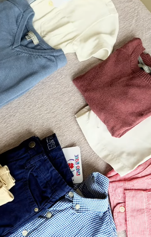 Conjunto de ropa sobre una superficie clara, que incluye camisetas de diferentes colores, suéteres y pantalones. Los colores predominantes son azul, blanco, rojo y cuadros. Ideal para la temporada de primavera.