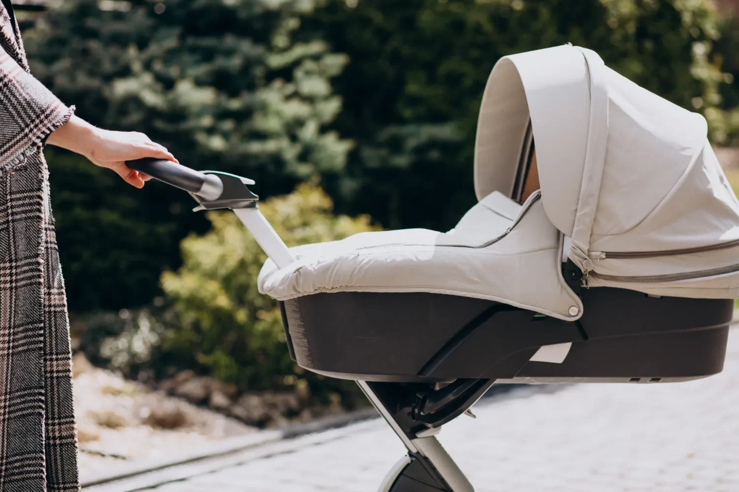 Carrito de bebé moderno en un entorno natural, con una mano agarrando el manillar, ideal para paseos al aire libre.